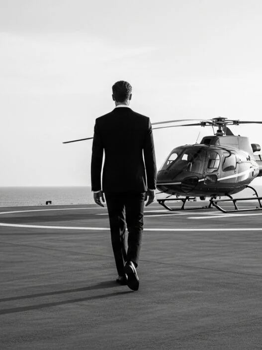 "Luxury travel singles over 40 – elegant man in black suit walking toward private helicopter on seaside helipad