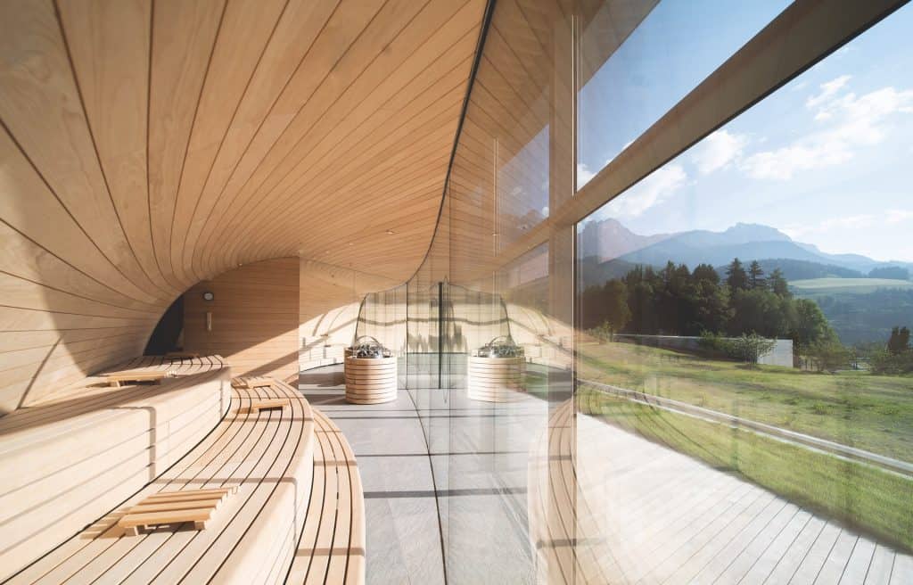 Luxury wellness retreats 2025 - Hotel Krallerhof innovative Alpine sauna with curved wooden architecture, panoramic mountain views, and modern glass design for high-altitude wellness training